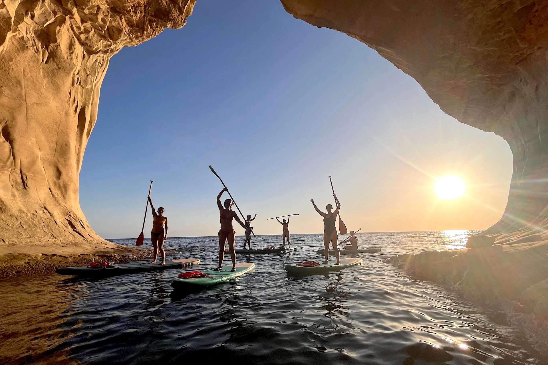 grupo practicando stand up paddle en una cueva al atardecer