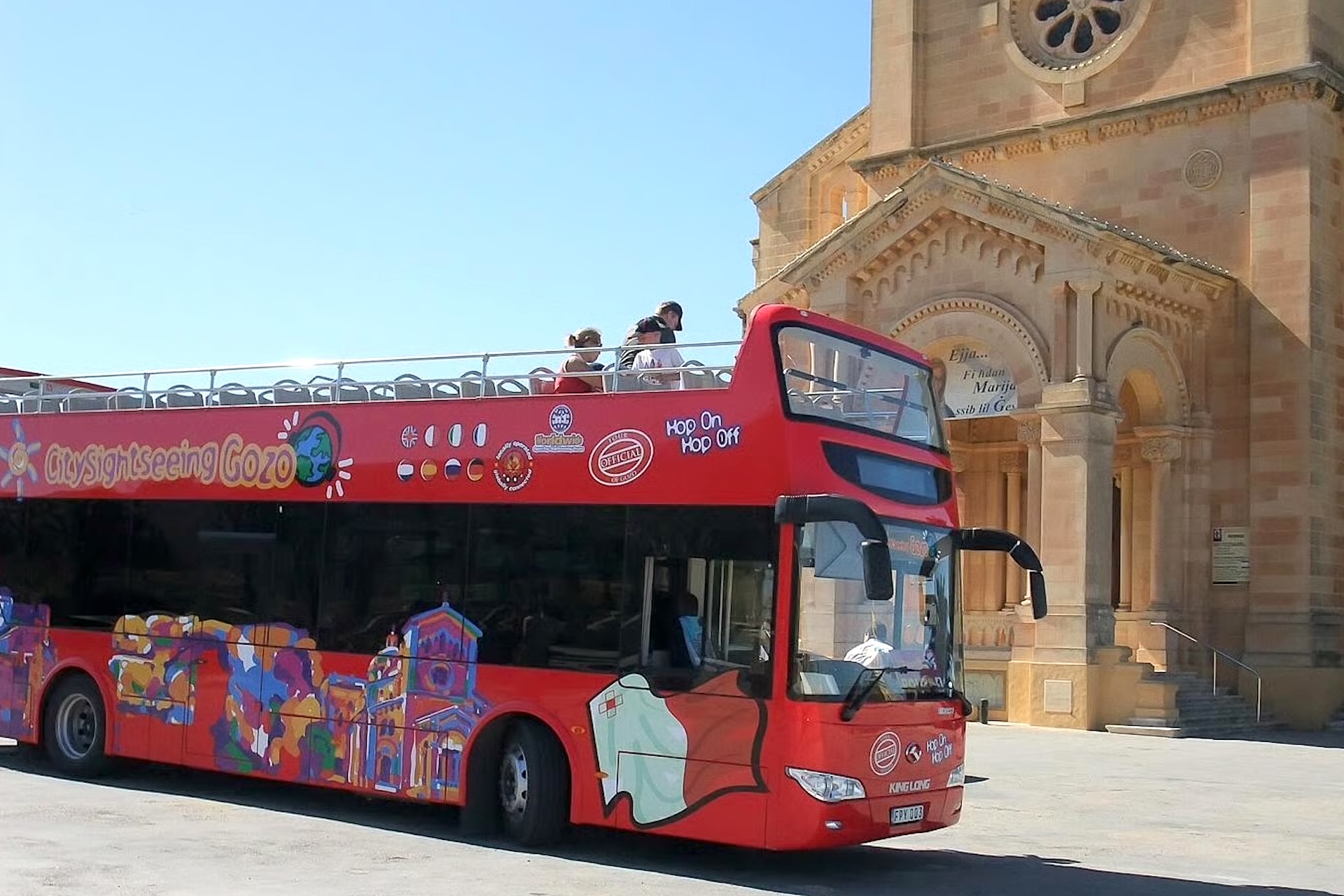 autobus rosso hop-on hop-off davanti a una chiesa a Gozo