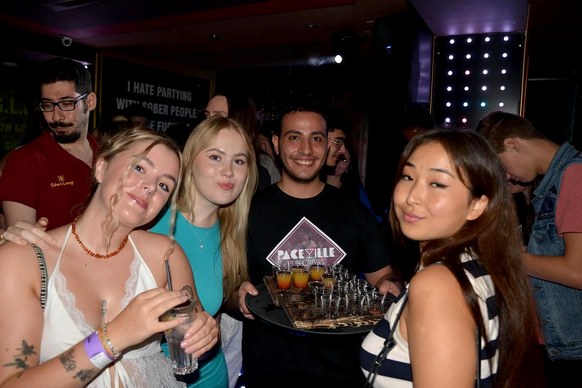 Trois jeunes femmes et un jeune homme avec un plateau de shooters à Paceville