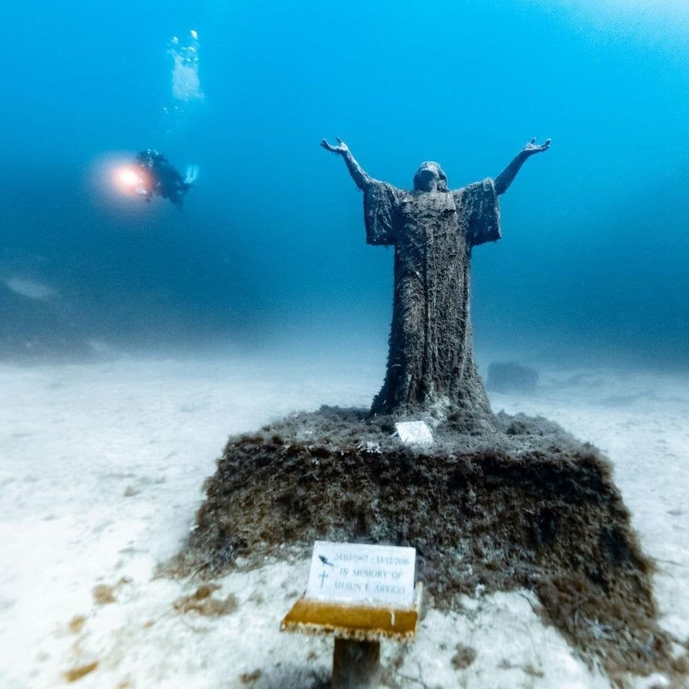 Underwater statue of Christ Diver beside the submerged statue of Christ off the coast of Malta