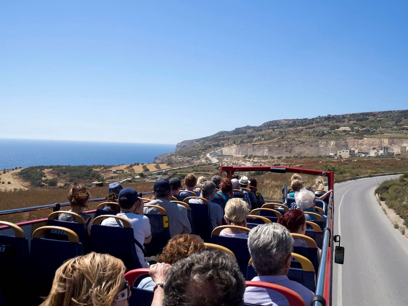 Autocarro turístico em Malta Passageiros no piso superior de um autocarro turístico descapotável ao longo de uma estrada costeira de Malta