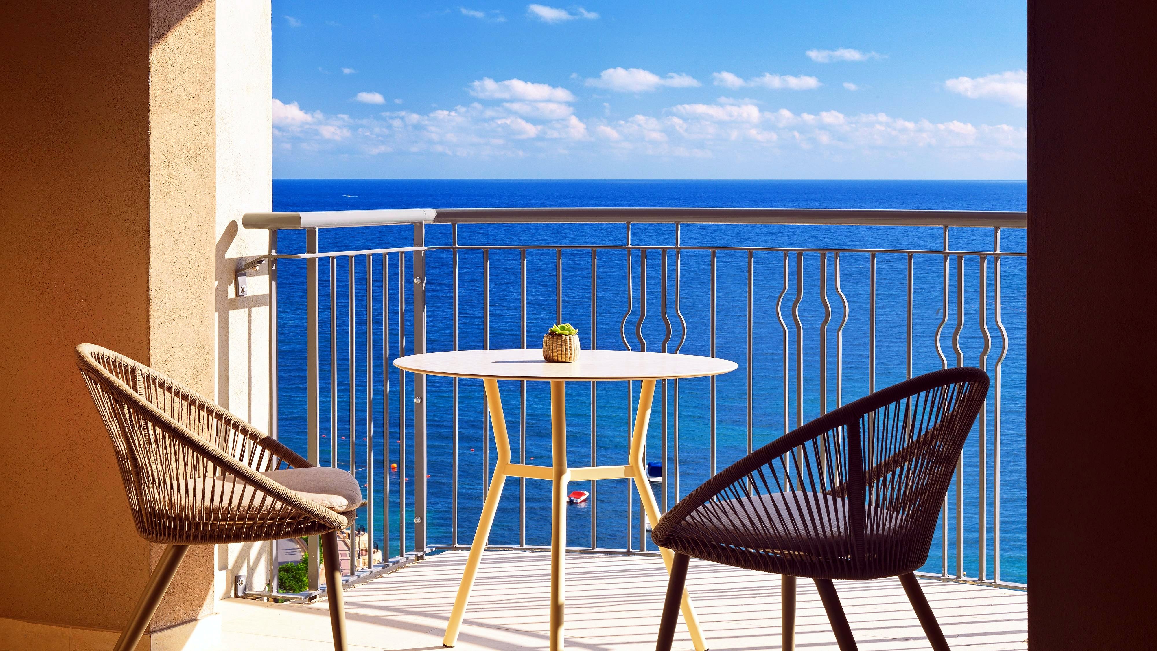 Balcon d’une suite avec table et fauteuils face à la mer au Malta Marriott Resort & Spa