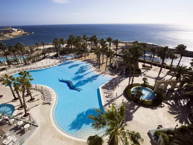 Vue plongeante sur la piscine principale du Hilton Malta, ses palmiers et la mer