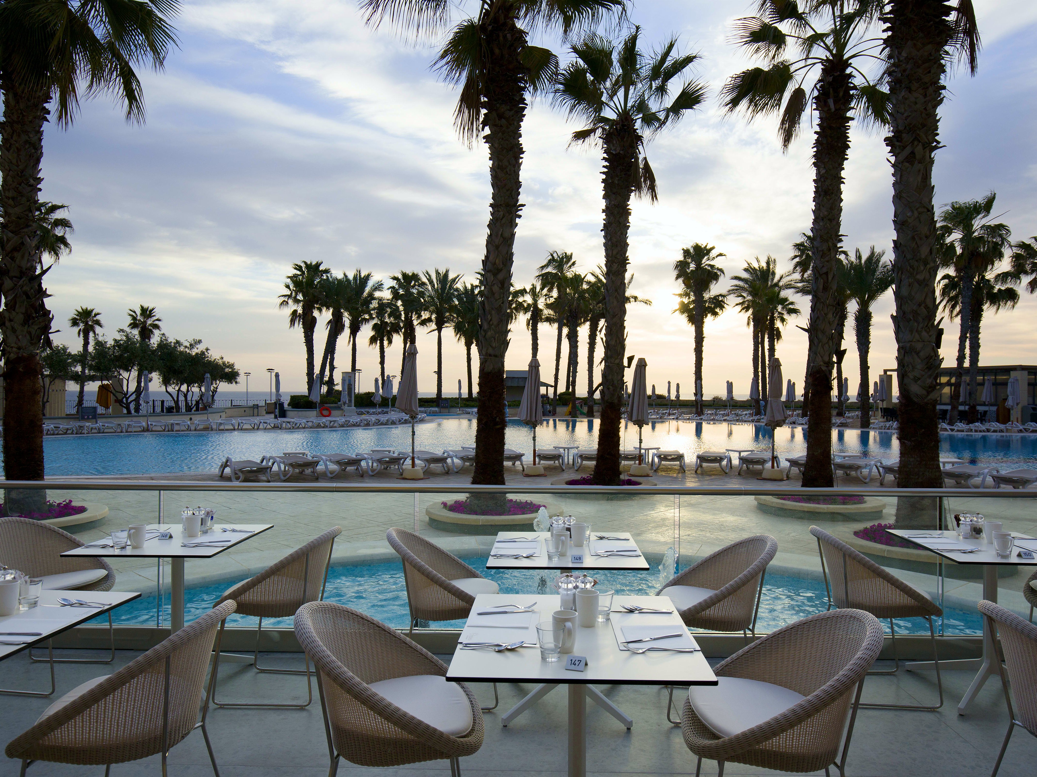 Tavoli apparecchiati sulla terrazza del ristorante Oceana di fronte alle piscine dell’Hilton Malta