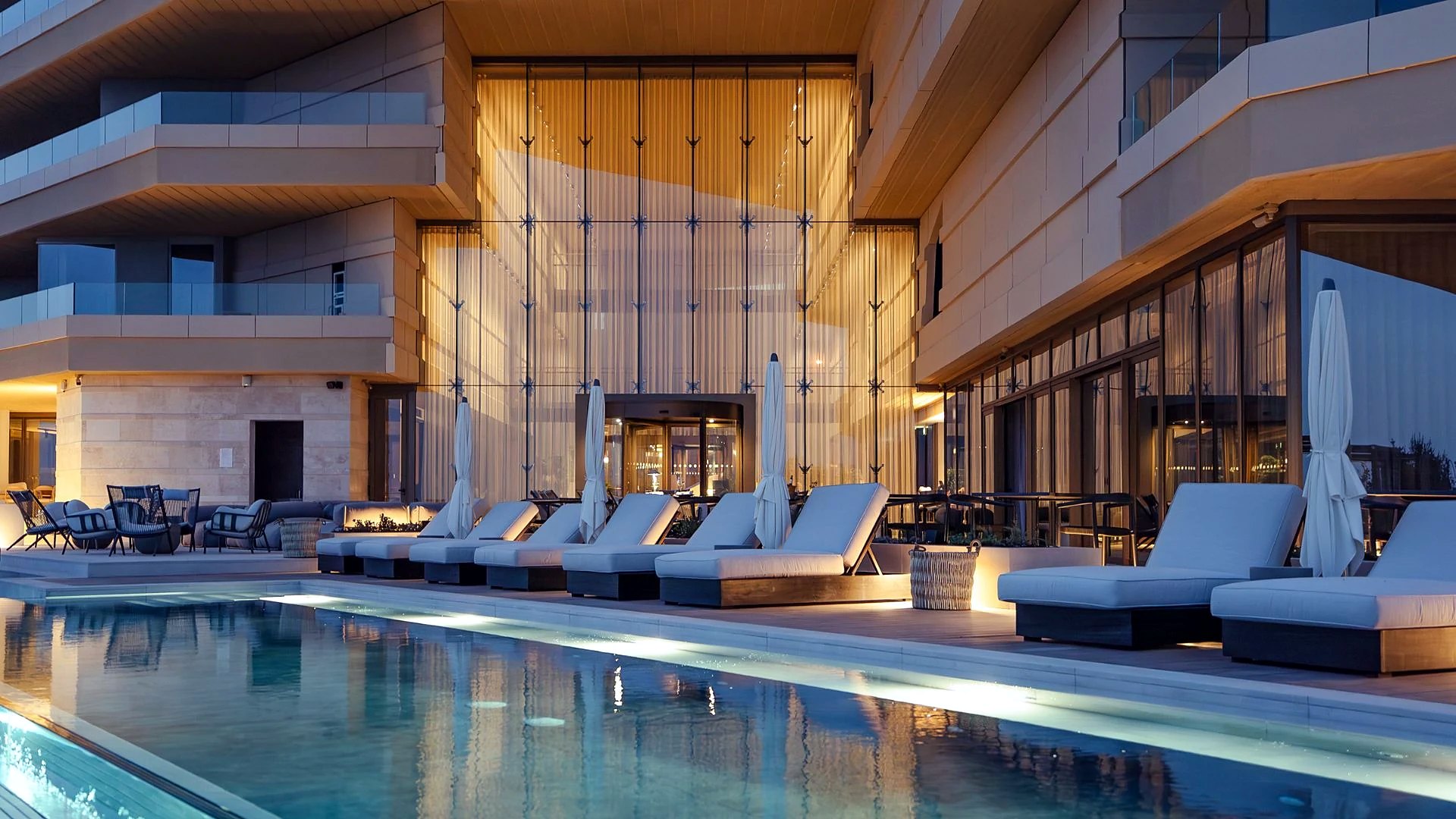 Piscina all’aperto e lettini davanti alla facciata vetrata del Verdala Wellness Hotel AX Privilege a Rabat, al calar della sera