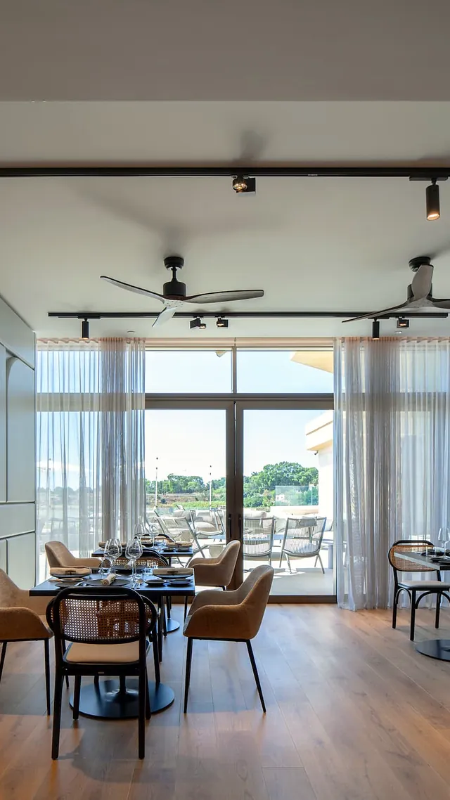 Salle lumineuse du restaurant The Griffin Brasserie au Verdala Wellness Hotel AX Privilege, avec tables dressées et baie vitrée