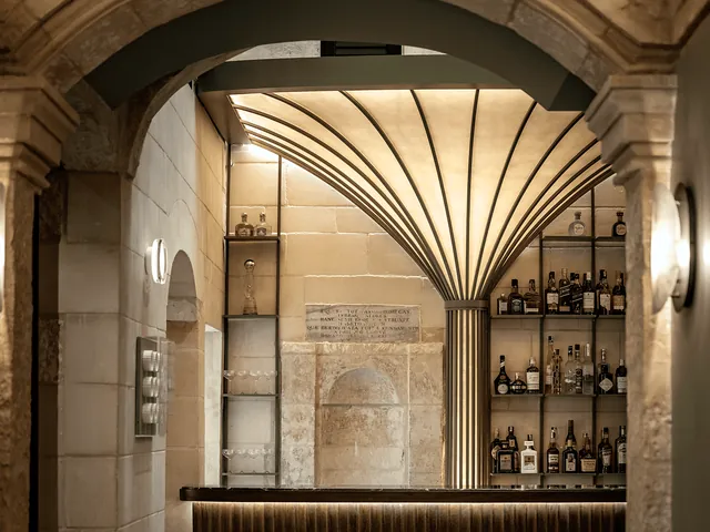 Bar à cocktails du Romègas Hotel sous une arche de pierre, avec un éventail lumineux et des étagères de bouteilles