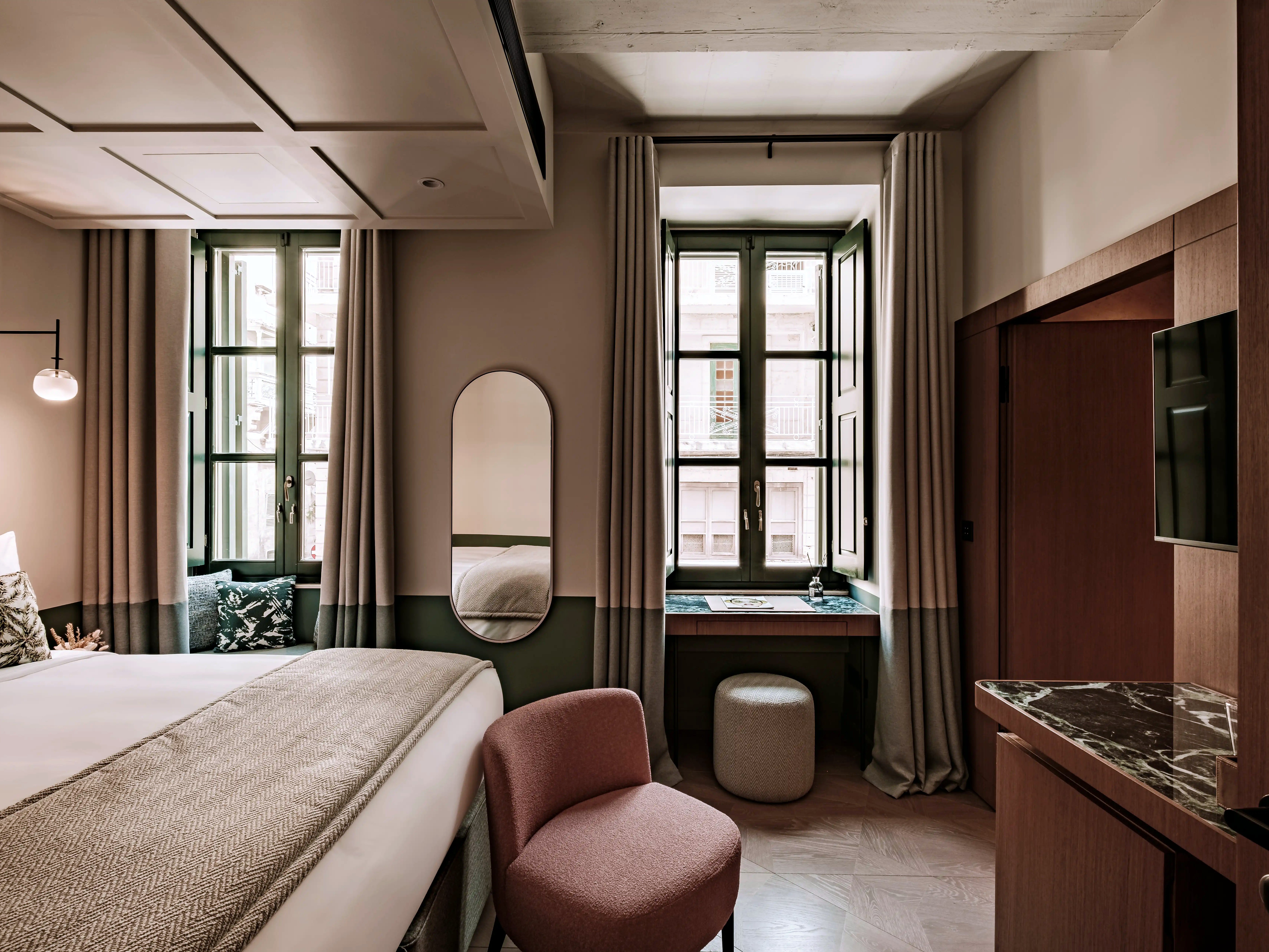 Quarto Deluxe do Romègas Hotel com cama grande, revestimentos em madeira e duas janelas para as ruas de Valeta