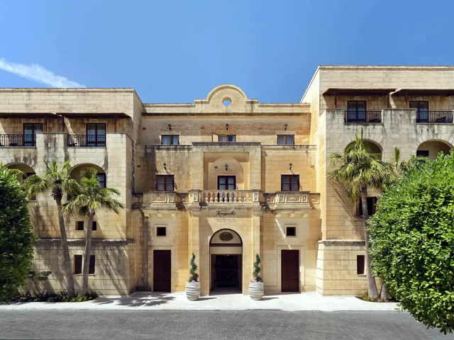 Façade en pierre calcaire et entrée principale du Kempinski Hotel San Lawrenz à Gozo, entre palmiers et haies