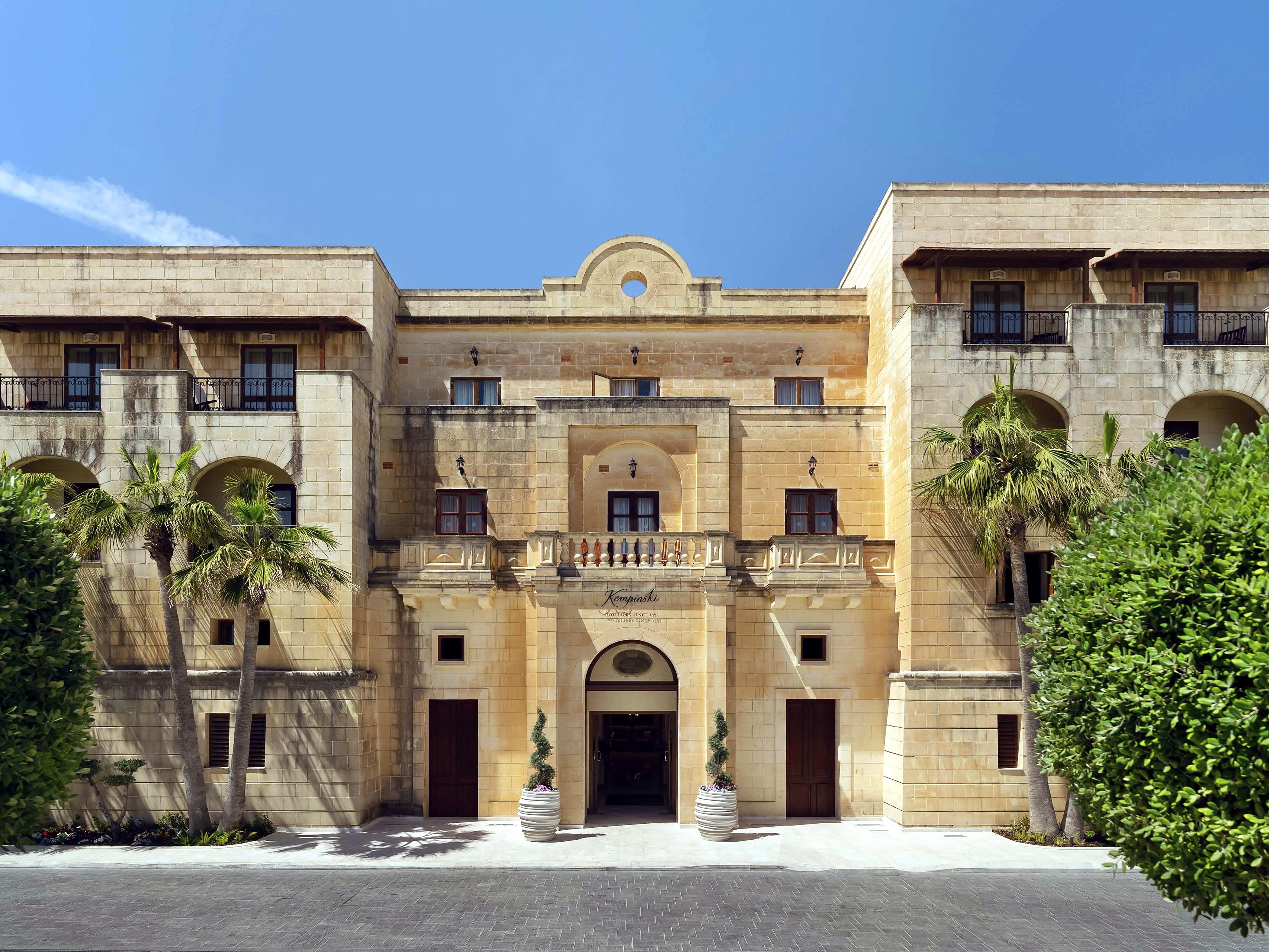 Facciata in pietra calcarea e ingresso principale del Kempinski Hotel San Lawrenz a Gozo, tra palme e siepi