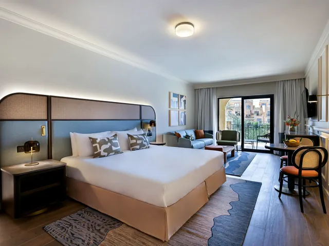 Chambre Grand Deluxe vue piscine avec grand lit, coin salon et porte-fenêtre sur balcon au Kempinski Hotel San Lawrenz