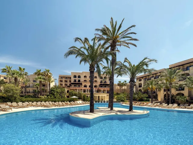 Grande piscine extérieure bordée de transats avec îlot de palmiers au Kempinski Hotel San Lawrenz à Gozo