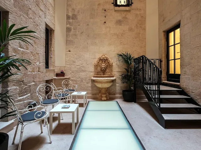 Cour intérieure en pierre du Palais Le Brun avec fontaine murale, escalier en fer forgé et sol en dalles de verre