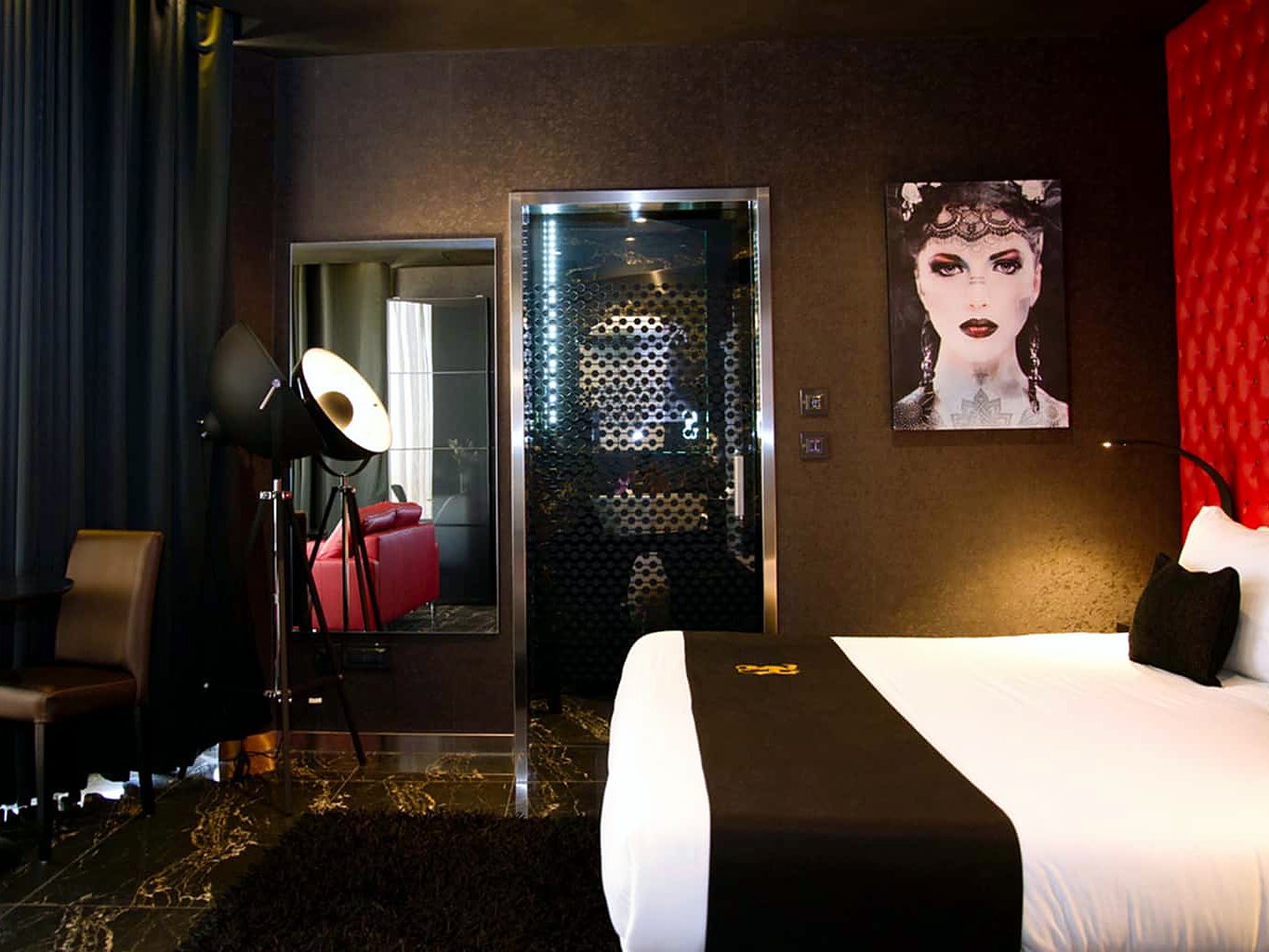 Camera dell’Hugo’s Boutique Hotel con testiera capitonné rossa, ritratto a parete e doccia in vetro