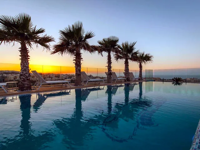 Palmiers et transats se reflétant dans la piscine à débordement du toit partagée par le Hugo’s Boutique Hotel
