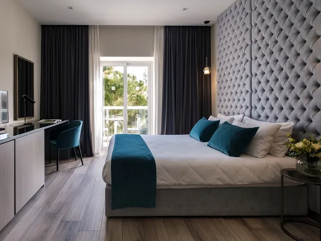 Chambre supérieure de l’Urban Valley Resort & Spa avec lit double, tête de lit capitonnée, bureau et porte-fenêtre sur le balcon