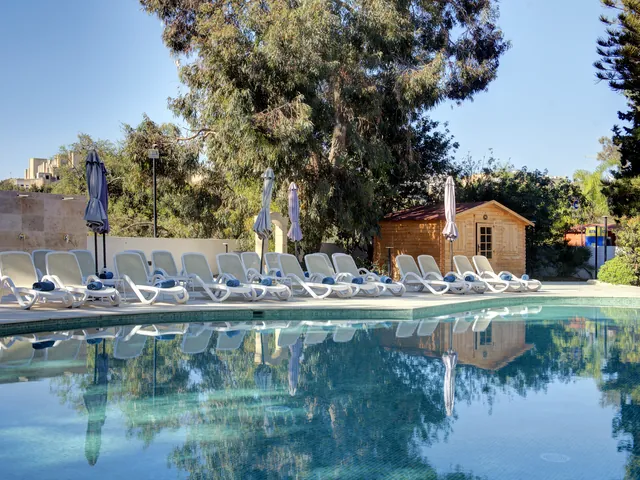 Piscine extérieure de l’Urban Valley Resort & Spa entourée de transats et d’arbres, au bord de la vallée de Wied Għollieqa