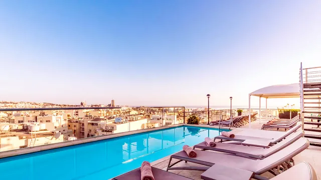 Piscine sur le toit de l’AX The Victoria avec ses transats et une vue sur les toits de Sliema