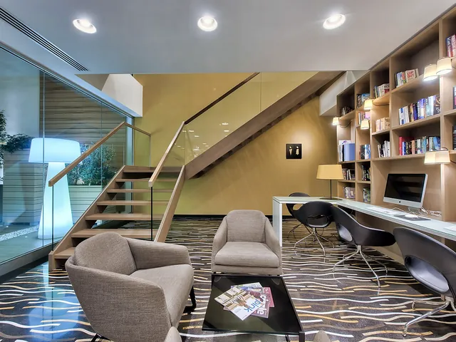 Coin bibliothèque avec fauteuils et ordinateurs en libre accès dans le hall de l’Hotel Valentina