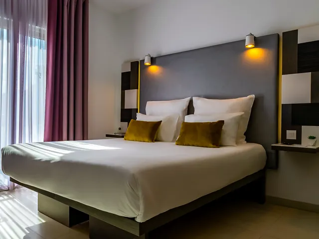 Grand lit et tête de lit éclairée dans une chambre supérieure de l’Hotel Valentina à St Julian’s