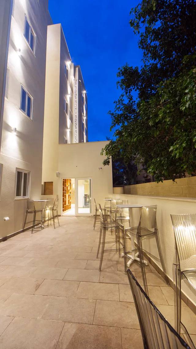 Terrasse arrière du Ddream Hotel éclairée le soir, avec tables hautes et tabourets transparents