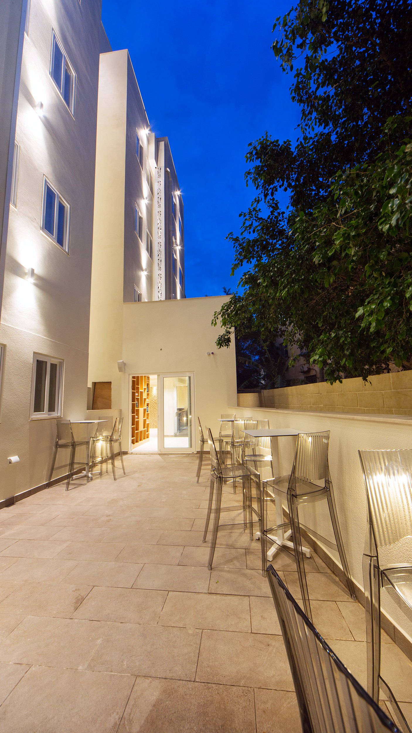 Terraza trasera del Ddream Hotel iluminada por la noche, con mesas altas y taburetes transparentes