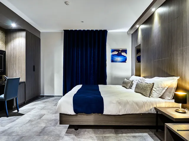 Chambre Deluxe du The District Hotel avec lit double, jeté bleu marine, bureau et rideaux bleus