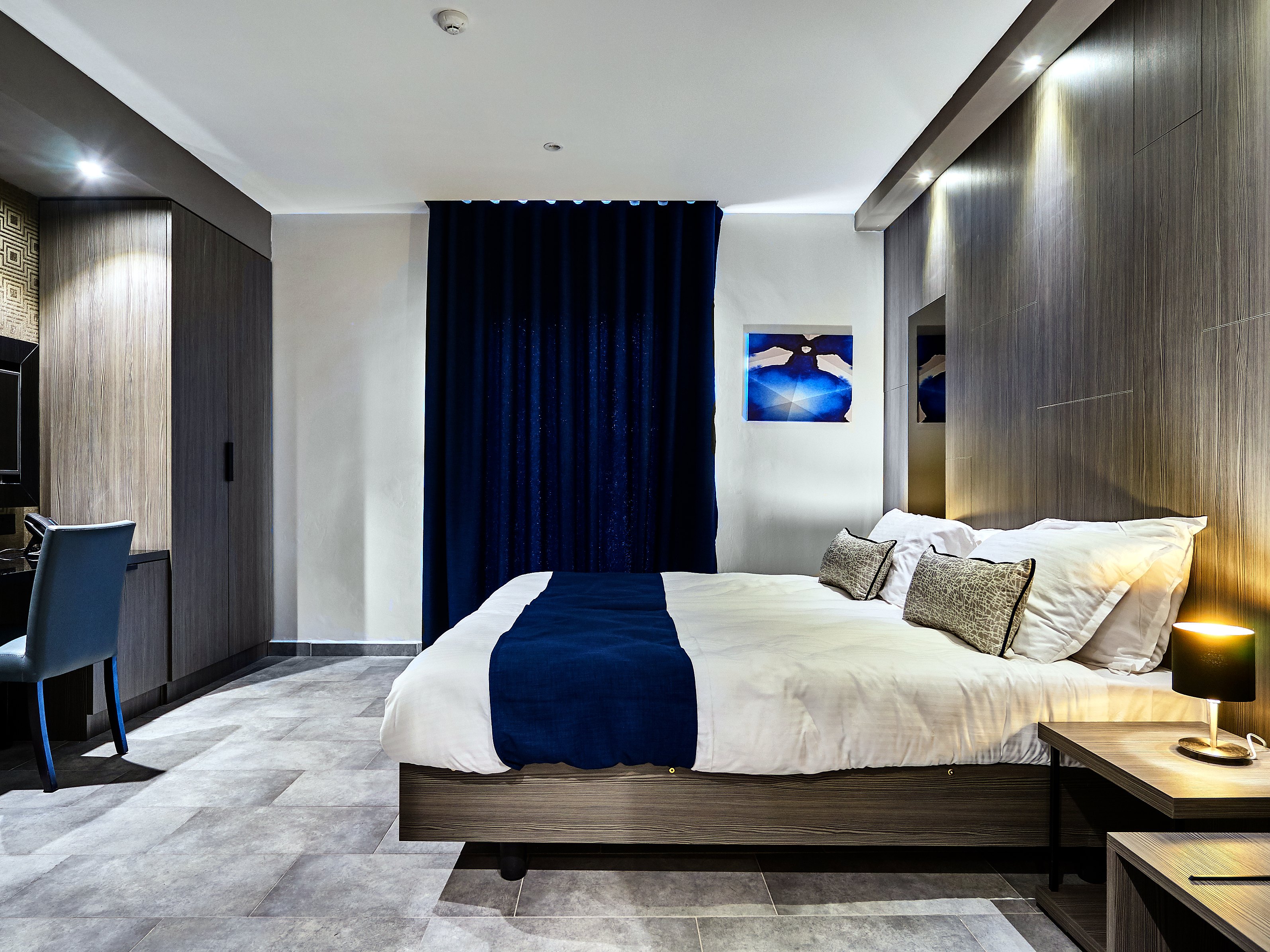 Camera Deluxe di The District Hotel con letto matrimoniale, copriletto blu notte, scrivania e tende blu