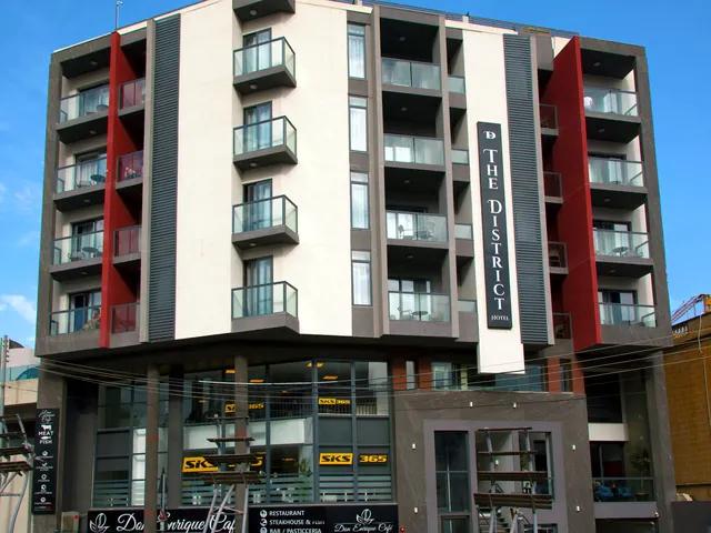 Façade blanche et grise du The District Hotel à St Julian’s, avec ses balcons vitrés et son enseigne verticale