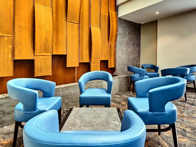 Lounge du The District Hotel avec fauteuils bleus, sol en marbre et mur décoratif en bois cuivré