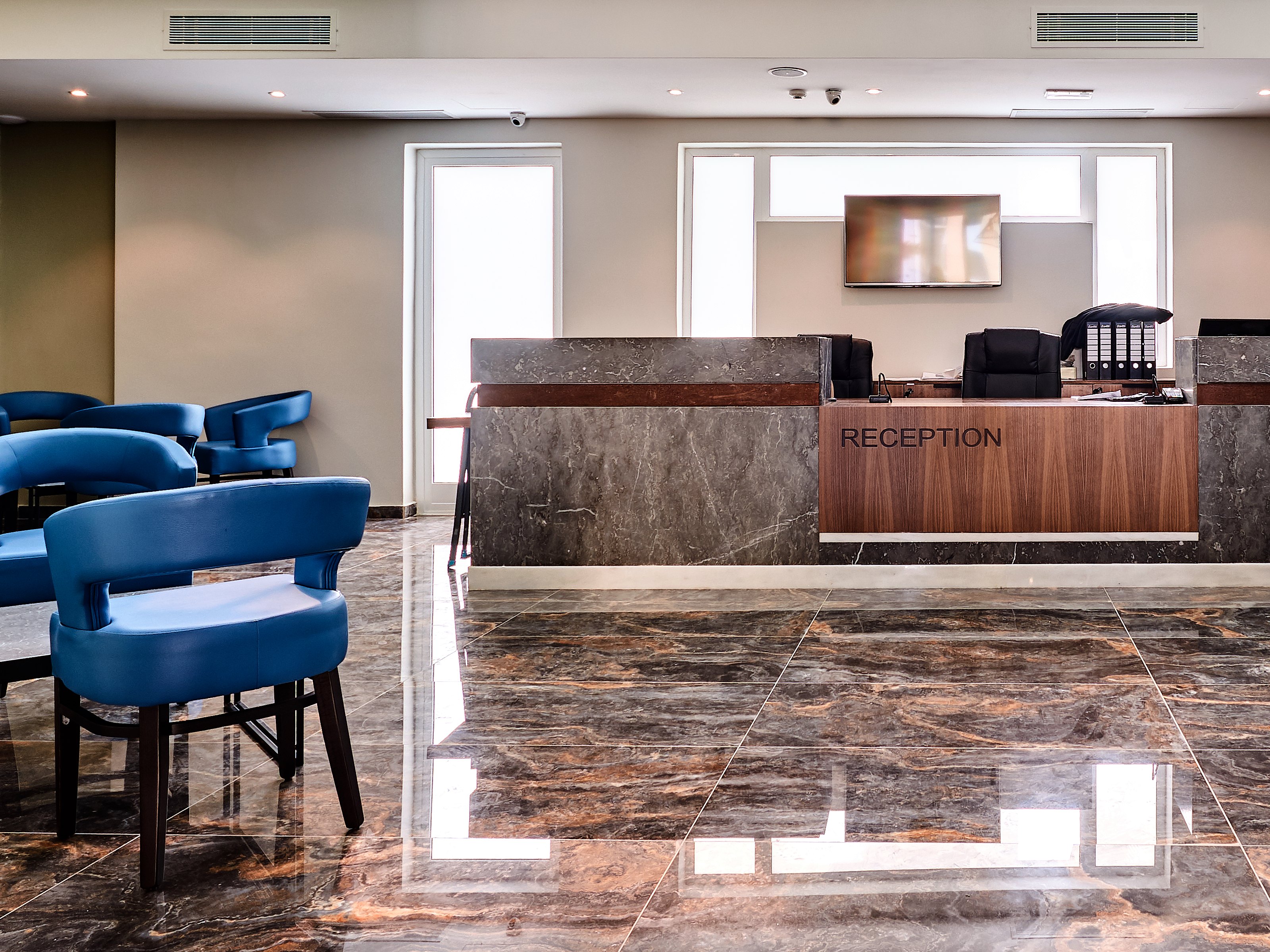 Hall della reception di The District Hotel con bancone in marmo e legno, pavimento lucido e poltrone blu