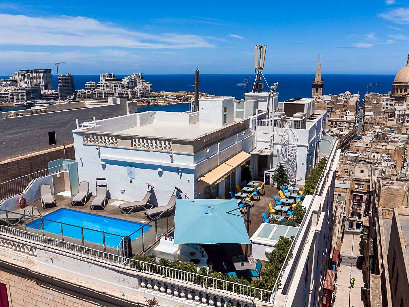 Piscina e lettini sulla terrazza sul tetto dell’Osborne Hotel, affacciata sui tetti di La Valletta e sul mare