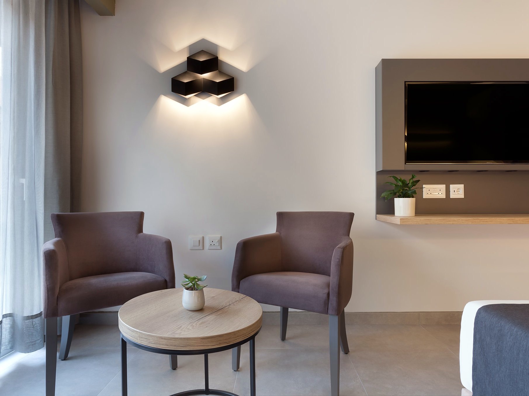 Coin salon d’une chambre Deluxe de l’Azur Hotel by ST Hotels avec deux fauteuils, table ronde et télévision