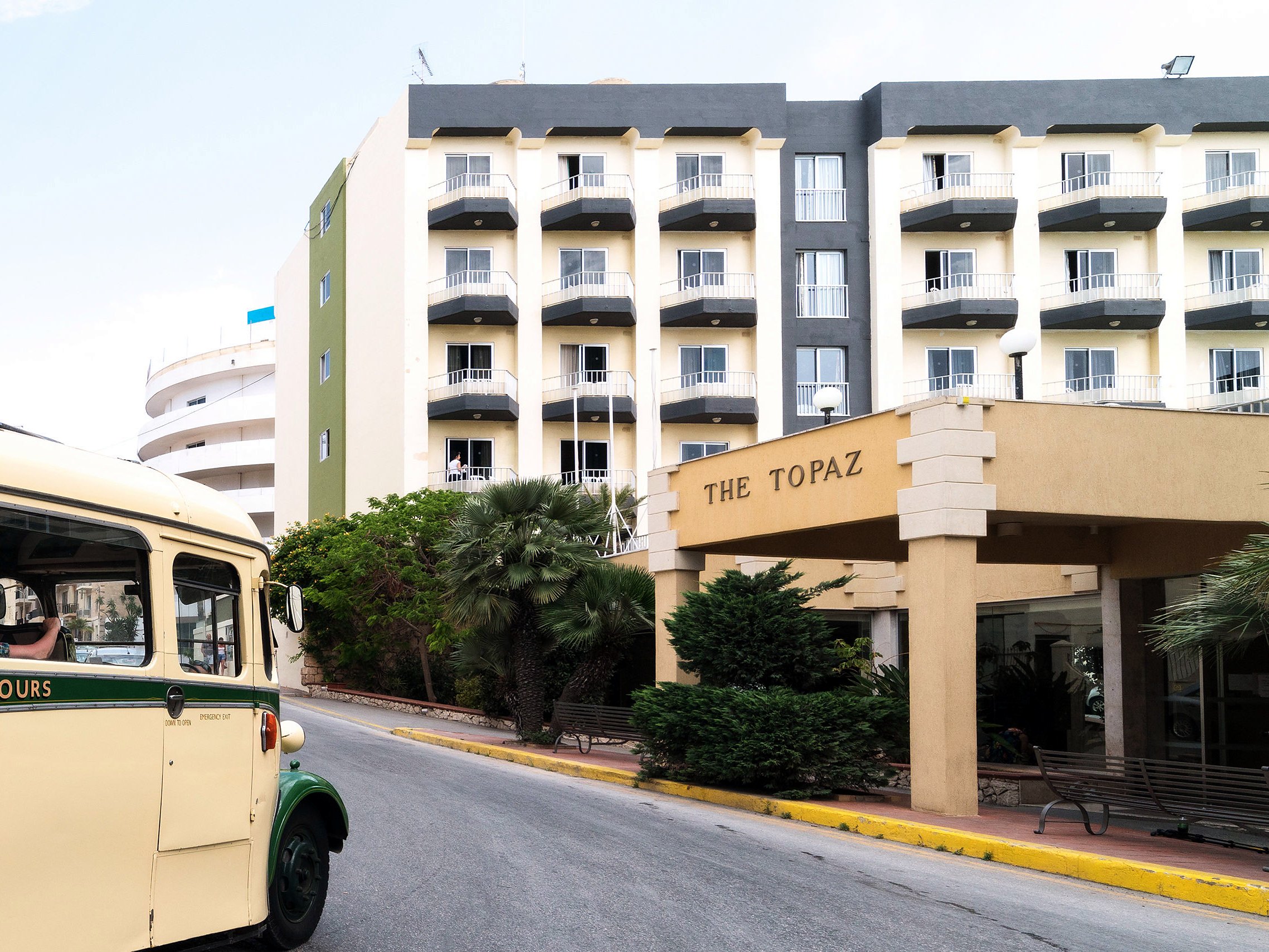 Topaz Hotel - Facciata Facciata del Topaz Hotel a Buġibba con l’ingresso «The Topaz», i balconi e un autobus d’epoca parcheggiato davanti