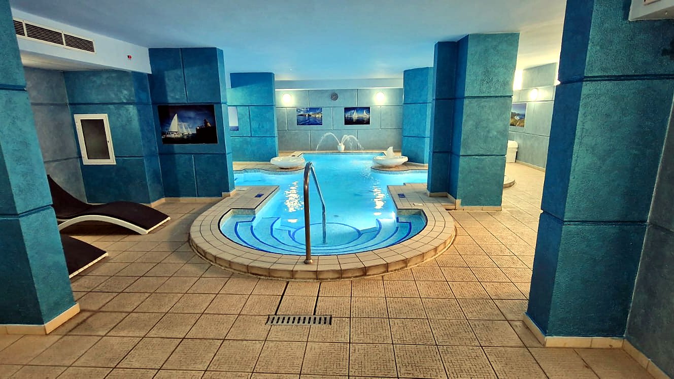 Piscina interna del Topaz Hotel circondata da colonne blu e lettini