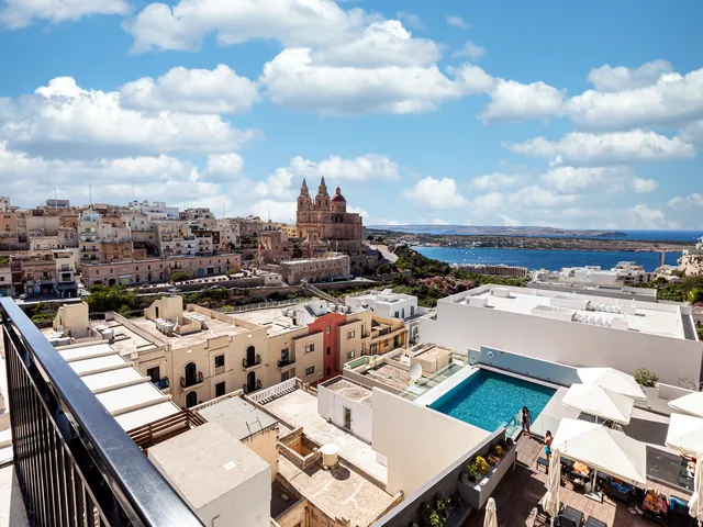 Vue depuis un balcon du Pergola Hotel & Spa sur sa piscine, l’église et la baie de Mellieħa