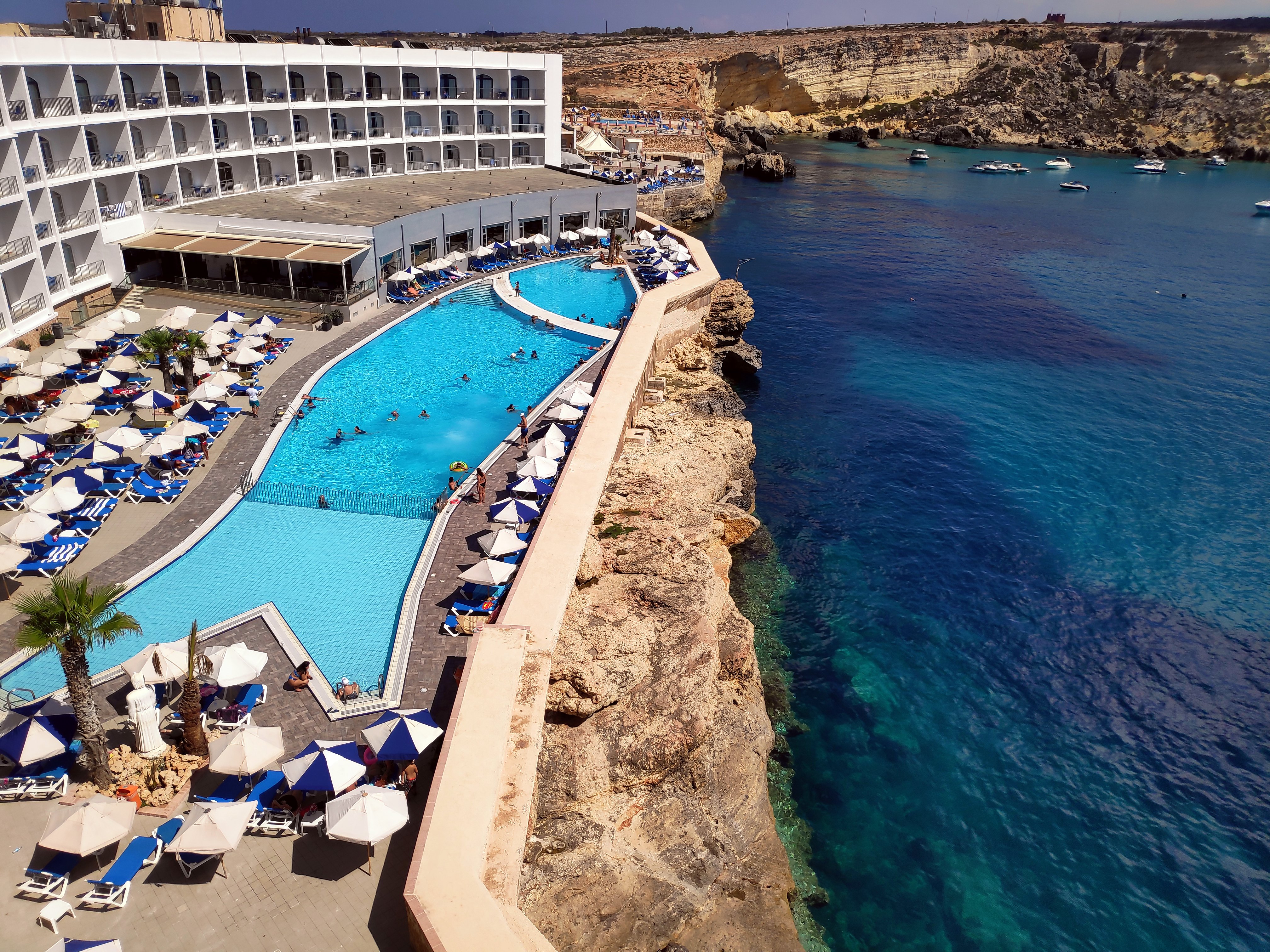 Piscina all’aperto del Paradise Bay Resort circondata da lettini, a ridosso delle scogliere e del mare