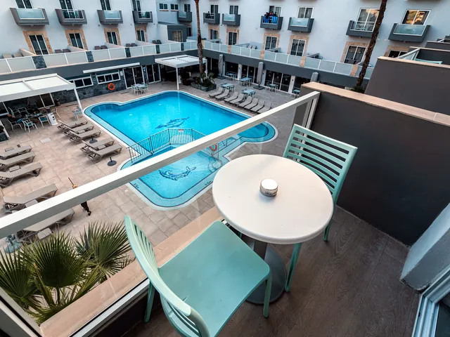 Piscine extérieure du Pebbles Resort vue d’un balcon, entourée de transats au pied des façades de l’hôtel
