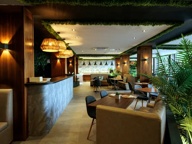 Salle du restaurant Flavours du Pebbles Resort avec comptoir en pierre, banquettes, plantes vertes et suspensions en osier