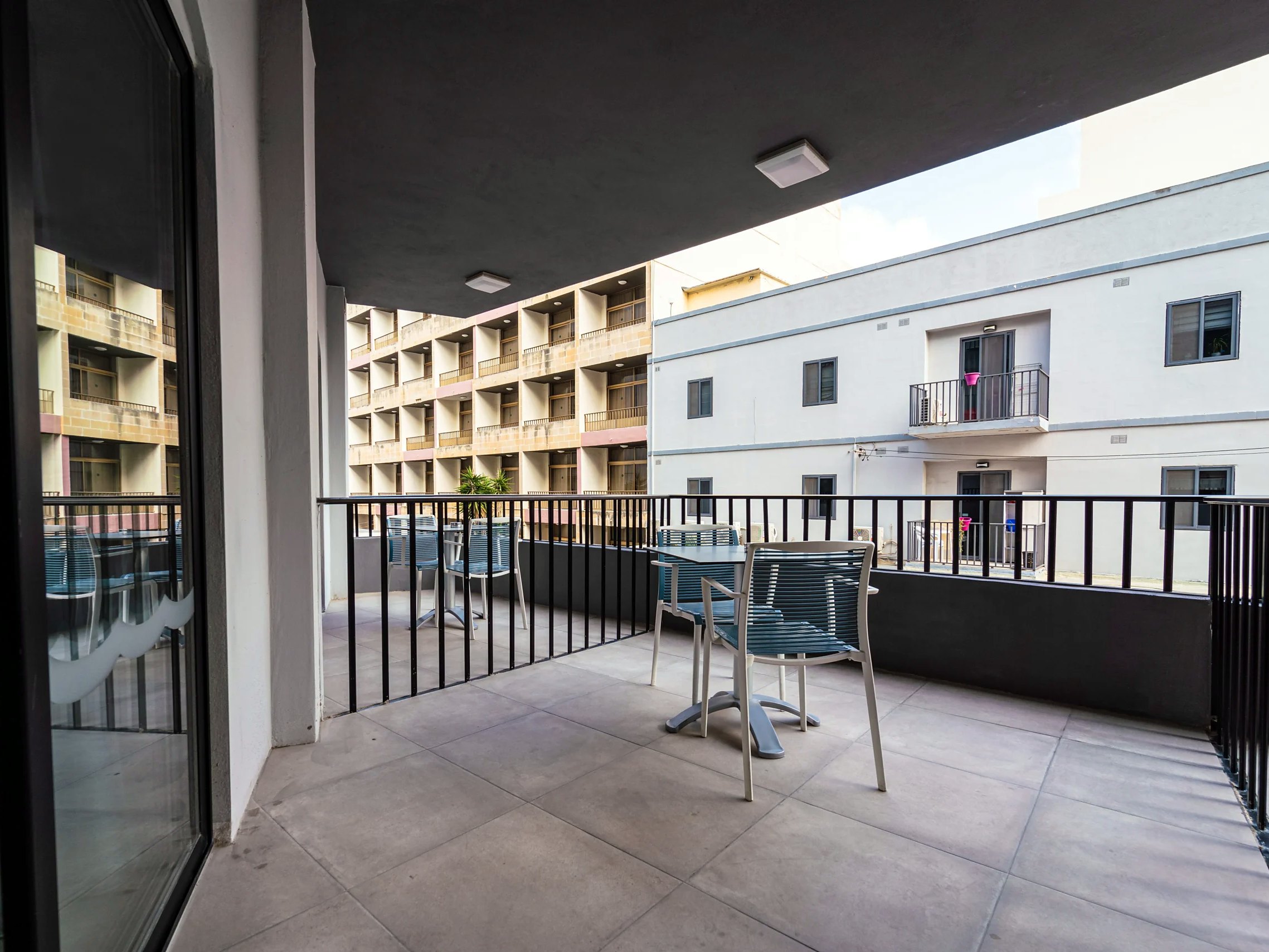 Ampia terrazza privata di una camera del Pebbles Resort con tavolo e sedie, di fronte ai palazzi vicini