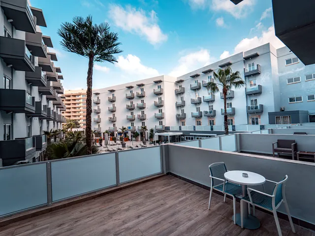 Vue d’ensemble du Pebbles Resort depuis une terrasse, sur les façades blanches à balcons, les palmiers et la cour de la piscine