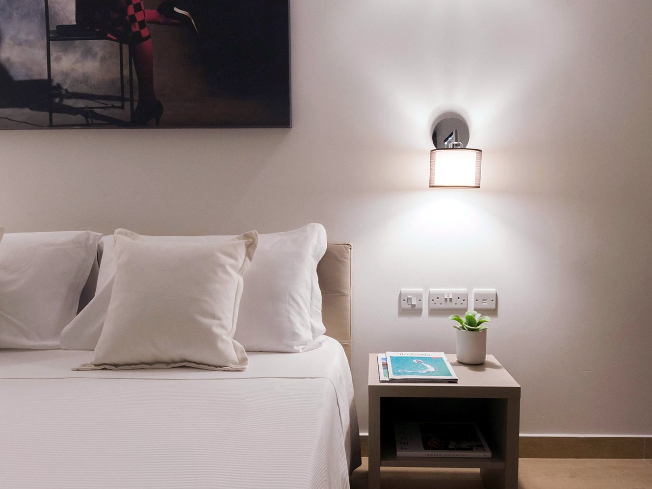 Cama de matrimonio y mesita de noche de una habitación superior reformada del Alexandra Hotel en St Julian’s