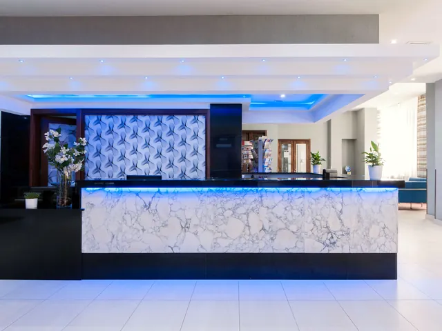 Comptoir de la réception de l’Alexandra Hotel en marbre blanc éclairé de bleu, dans le hall rénové
