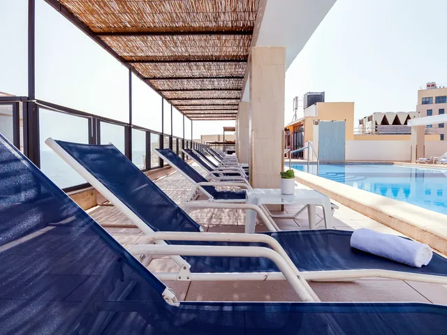 Transats bleus alignés sous une pergola en canisse au bord de la piscine sur le toit de l’Alexandra Hotel
