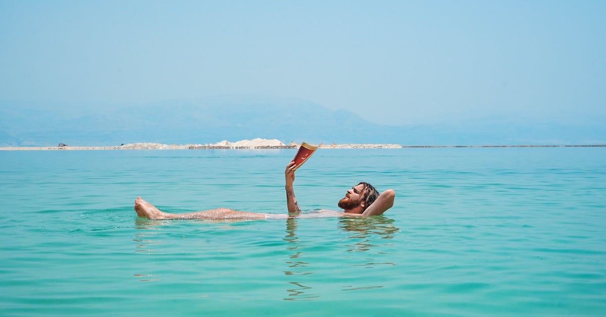 Learning English in the sun in Malta White man floating in the sea while reading a book