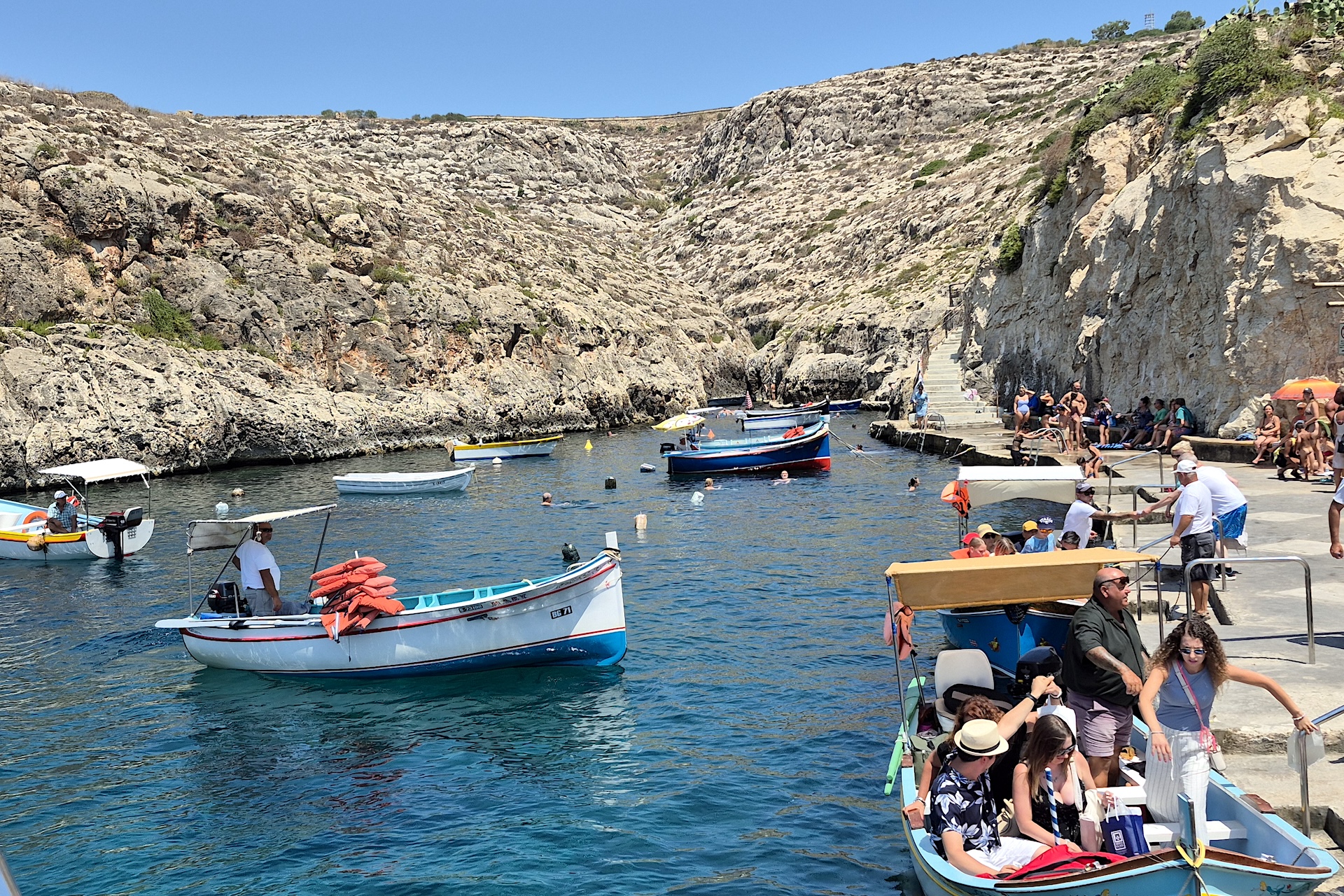 Pequenos barcos tradicionais e turistas na enseada de Wied iż-Żurrieq, ponto de partida para a Blue Grotto em Malta