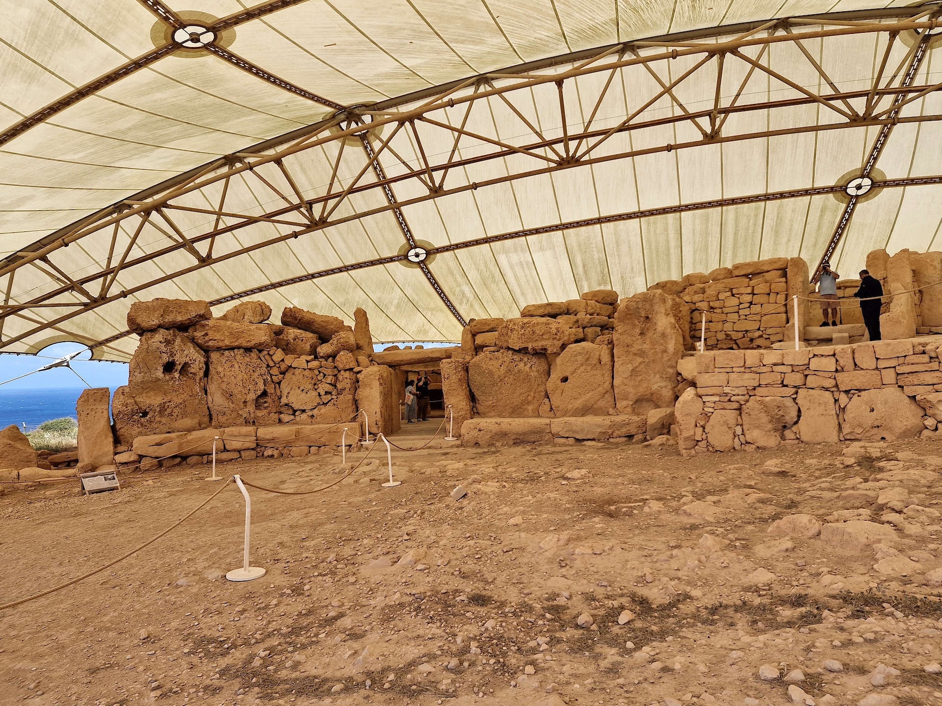 Intérieur du temple de Ħaġar Qim et ses murs mégalithiques Intérieur du temple de Ħaġar Qim à Malte : murs mégalithiques en calcaire et porte sous l’abri de protection, la Méditerranée en arrière-plan