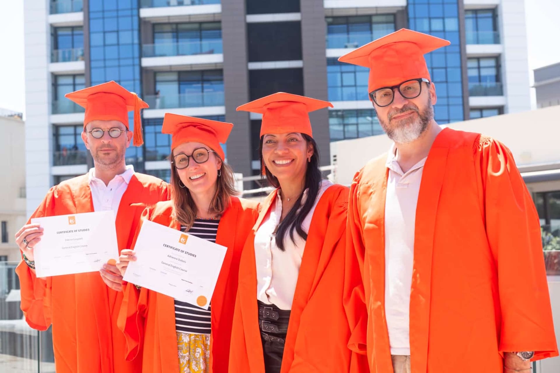 Adultes en toge orange avec leur certificat lors de la remise des diplômes d’EC Malta
