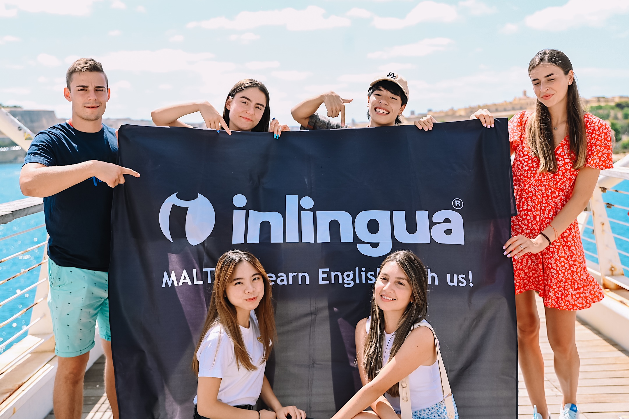 Студенческая жизнь в inlingua Malta Студенты inlingua Malta с баннером школы у воды