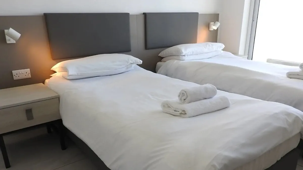 Residência ESE Claret – Quarto twin Quarto twin moderno da residência Claret com duas camas simples e iluminação mural